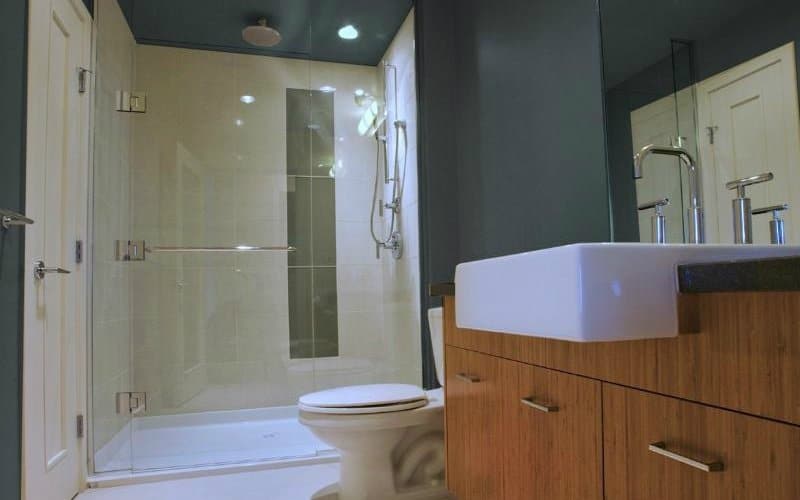 Shower with white tile walls in a bathroom that also has grey walls and a sink on a wooden vanity