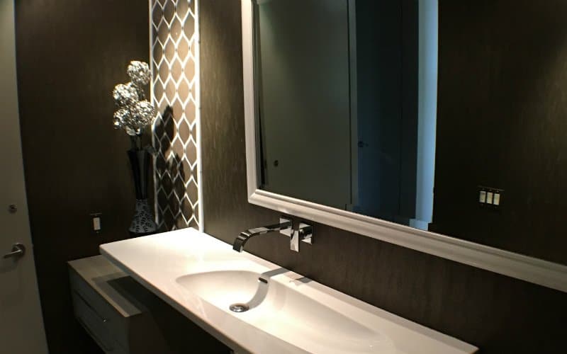 Large bathroom mirror set on a dark brown wall above a white, rectangular sink