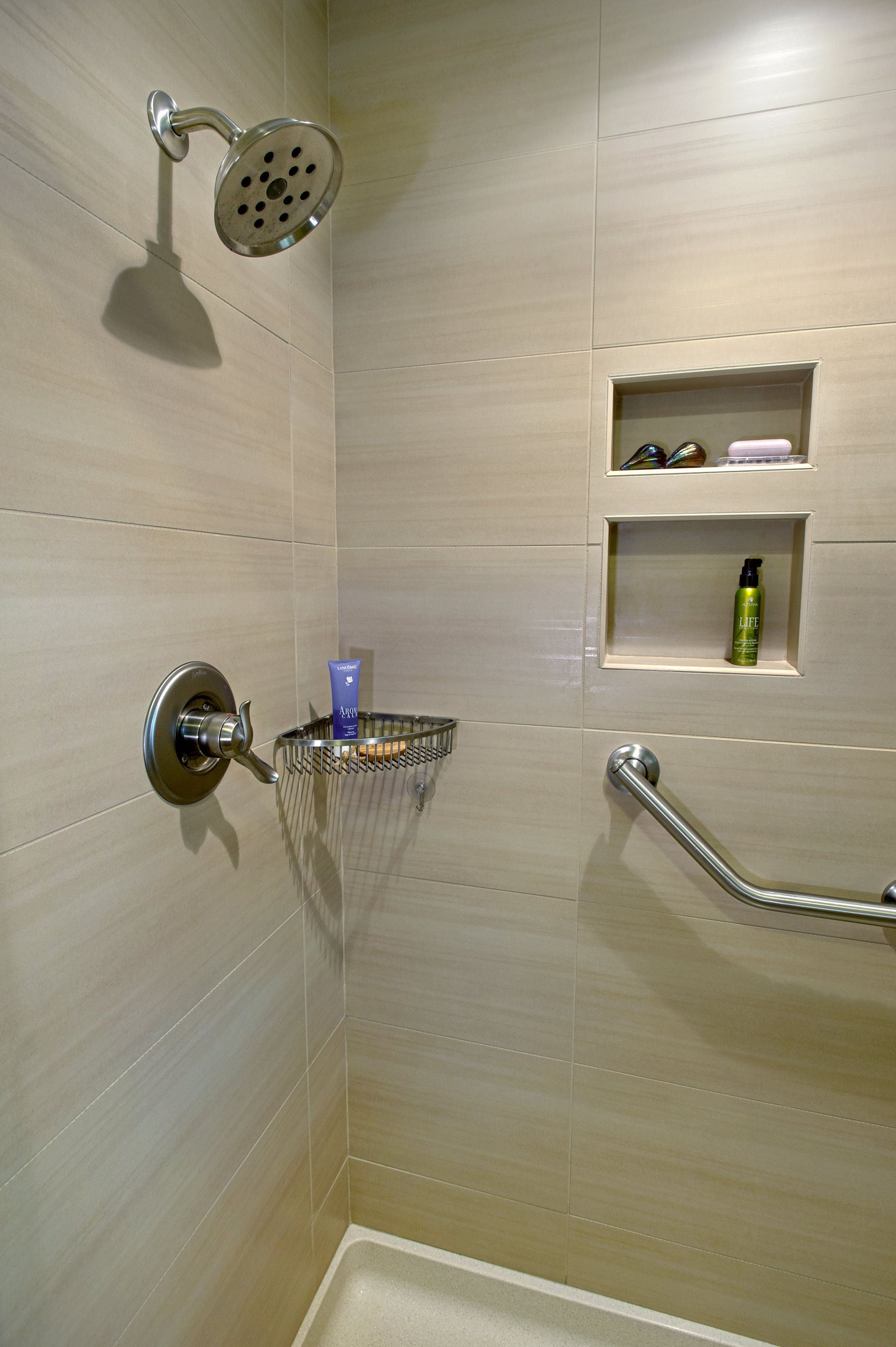 Shower with a small, silver storage basket mounted in the front right corner