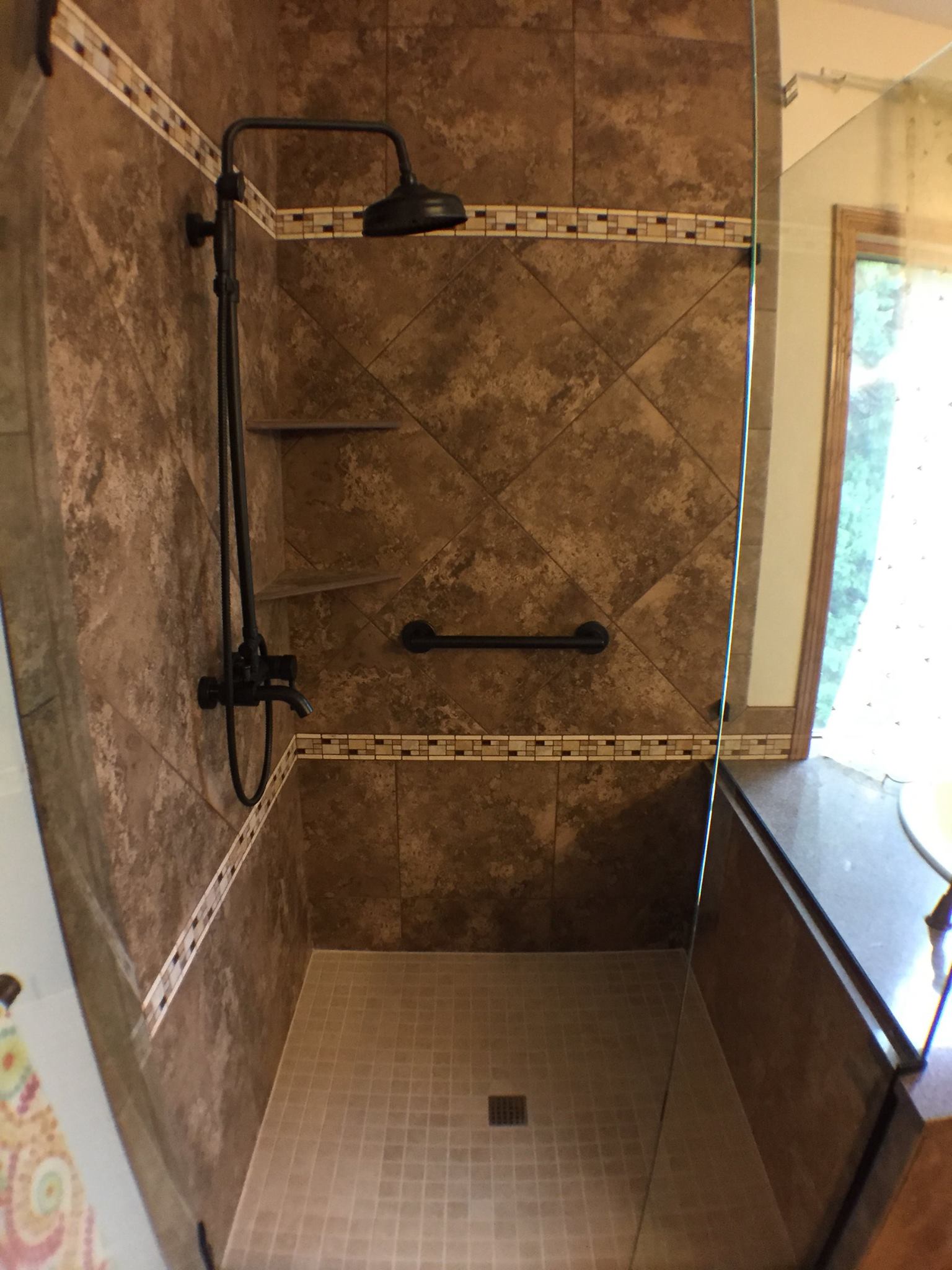 Shower with bronze fixtures, dark brown marble tile, and tan glass tile accents 