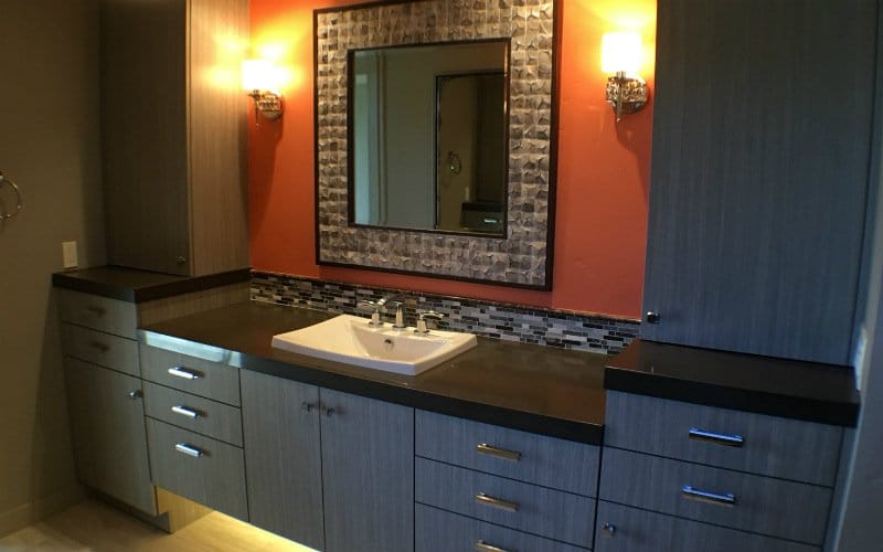 Vanity with grey cabinetry, tile, and a large mirror on a burnt orange wall
