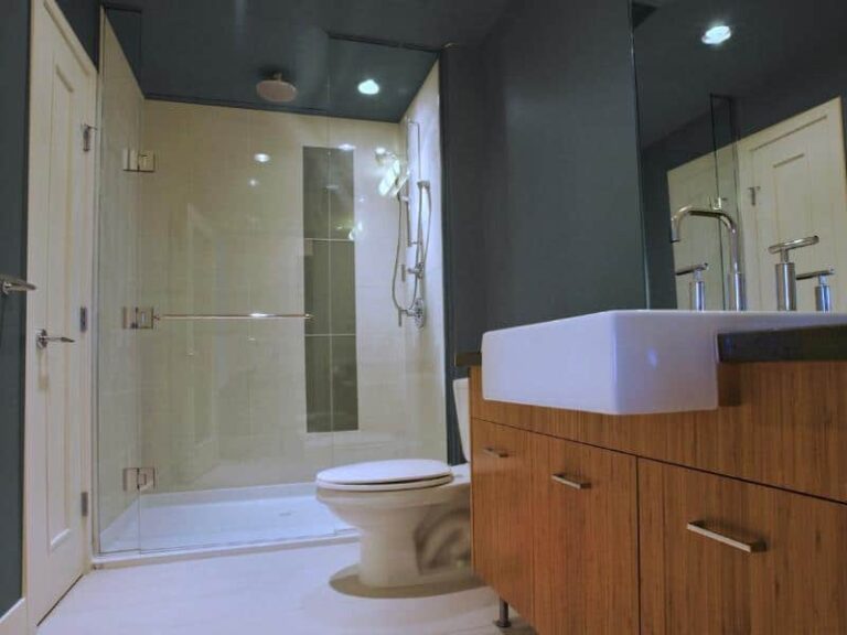 Glass doors on shower with ceiling mounted rain head shower and farmhouse sink